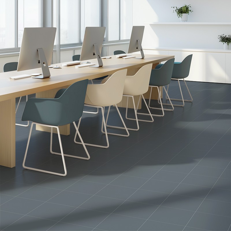 Matte anthracite grey tile, square format with thin joints forming a grid; in a modern office with a long wooden table, blue and cream chairs, monitors and windows that flood with light.