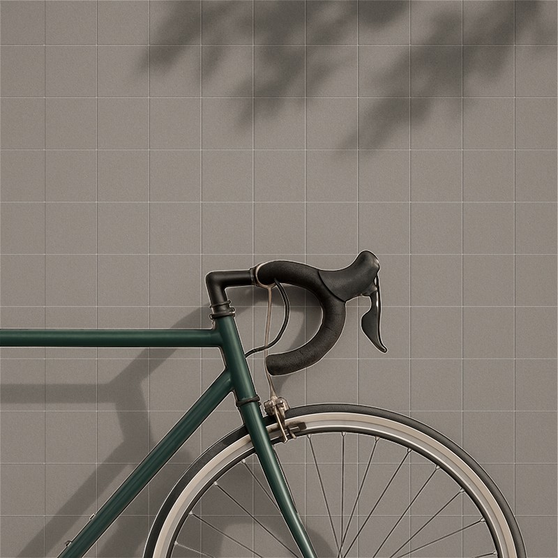 Carrelage gris clair à petits carreaux réguliers; au premier plan, le guidon et la roue avant d'un vélo vert appuyés contre le mur, ombre de feuillage projetée.