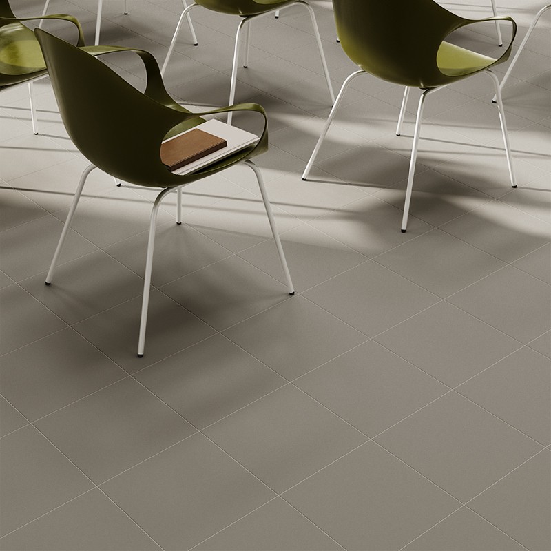 Quadratische, matte graue Bodenfliesen; Umgebung: moderne olivgrüne Stühle mit weißen Metallbeinen, ausgeprägte Schatten, auf einem Sitz liegt ein geschlossenes braunes Notizbuch.