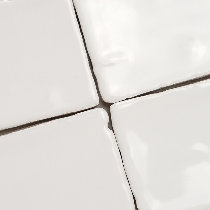 Bright white ceramic tiles (four) with dark joints forming a cross; irregular glaze, bevels and reflections, fitted in grout between them.