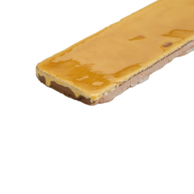 Élément rectangulaire mince beige, surface brillante jaune-orangé nappée, bords irréguliers et couches visibles, posé sur fond blanc dégagé.