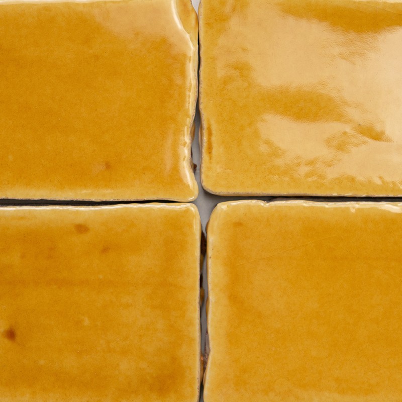 Azulejos amarelos brilhantes (quatro) — rejunte cinza formando cruz; superfícies esmaltadas com reflexos e cantos levemente arredondados.