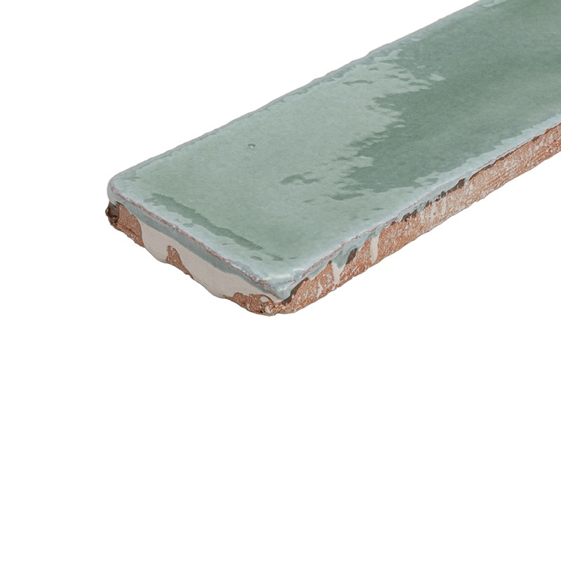 Light green glazed rectangular tile, irregular edge and exposed ceramic rim; isolated on white background, showing shiny texture and erosions at the base.