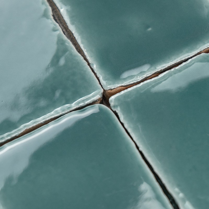 Four turquoise glazed tiles with narrow joints; glossy glaze shows small irregularities and a fine crack at the intersection, brown grout.