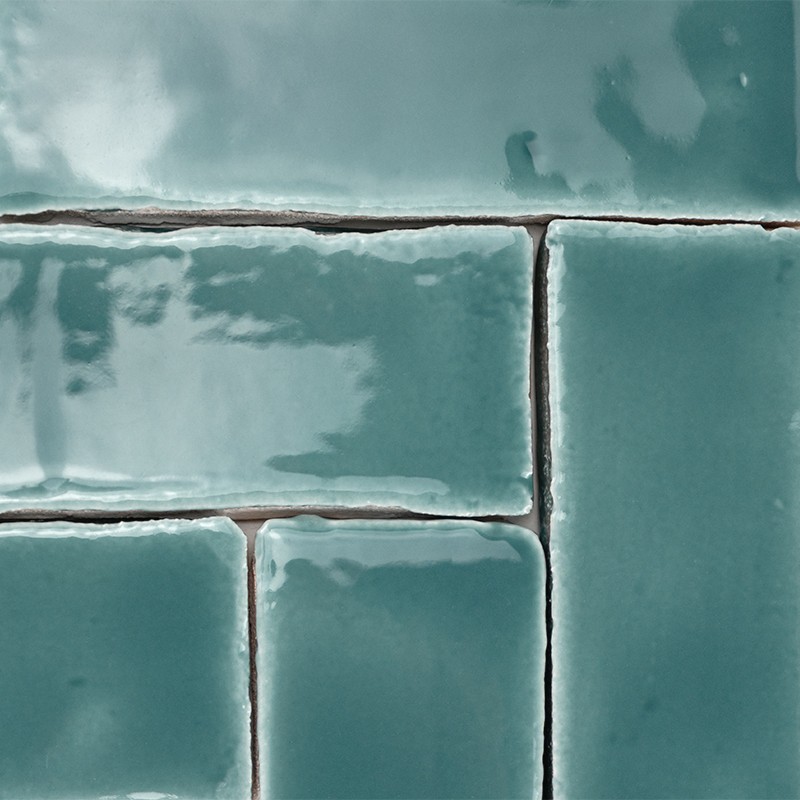 Bright turquoise rectangular ceramic tiles with dark grout lines and irregular glaze; arranged in a stepped pattern as part of a wall.