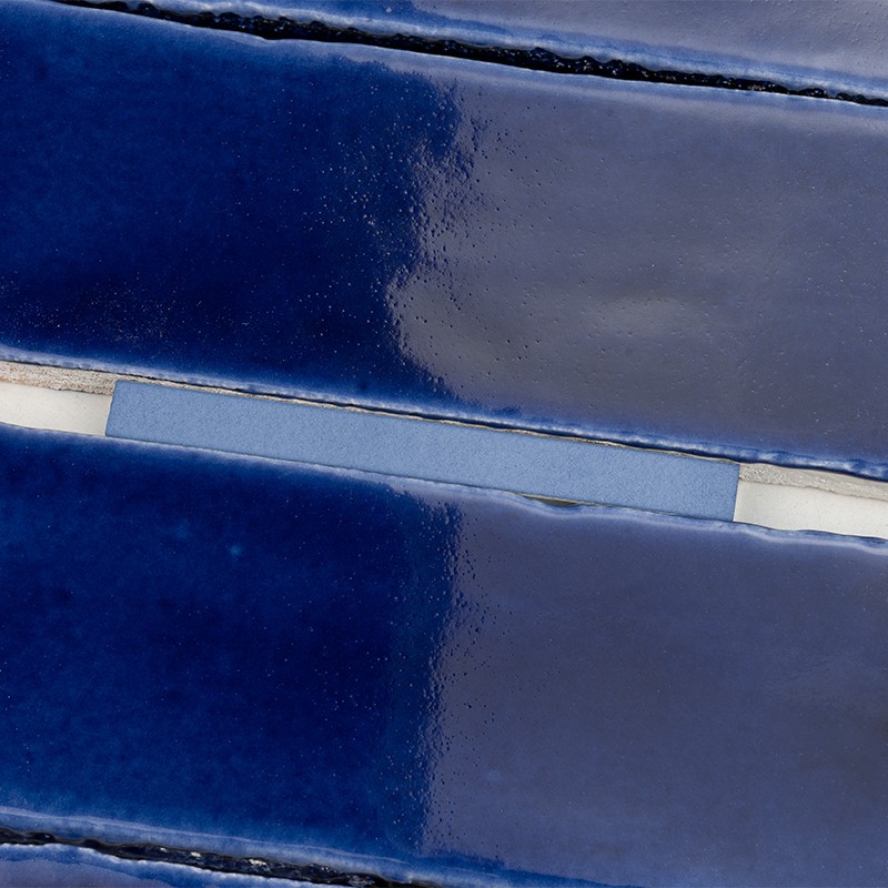 Azulejo cerâmico retangular azul escuro brilhante — fileiras com juntas estreitas e argamassa clara, superfície vidrada reflexiva com variações sutis de tonalidade.