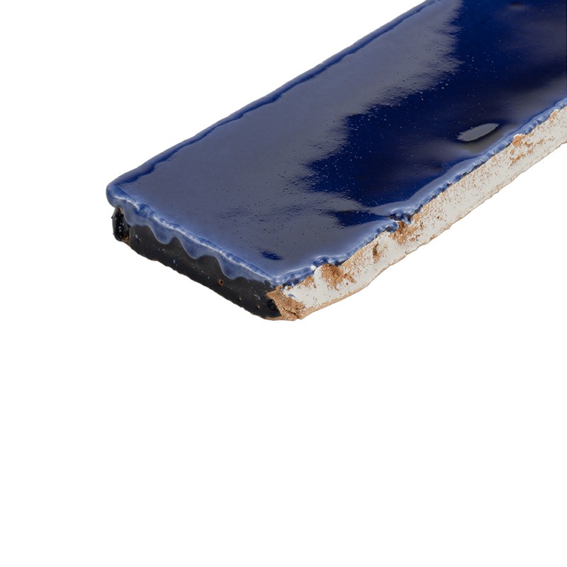 Azulejo retangular azul vívido com borda irregular e base cerâmica exposta; superfície vidrada brilhante, apoiado sobre fundo branco.