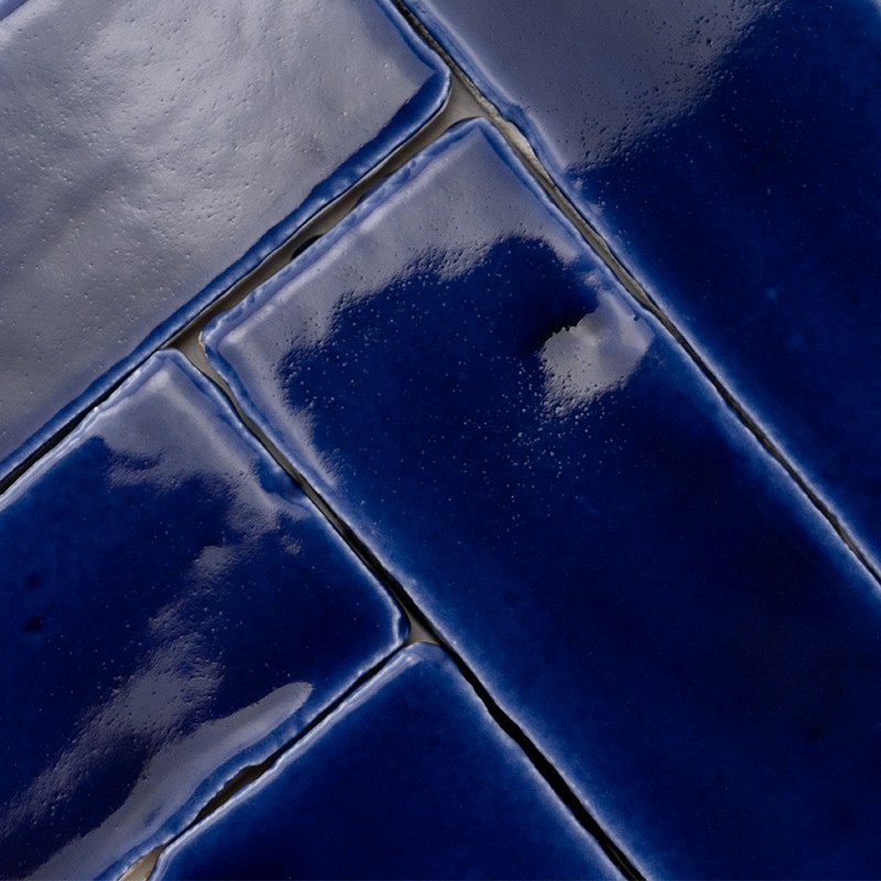 Azulejos cerâmicos azul-escuro brilhantes dispostos em padrão retangular; rejunte cinza entre peças, reflexos suaves de luz no esmalte.