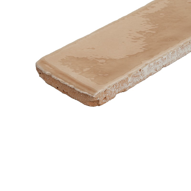 Azulejo rectangular beige esmaltado, superficie brillante y cantos irregulares; vista en ángulo que muestra el grosor y la base sin esmaltar, sobre fondo blanco aislado.