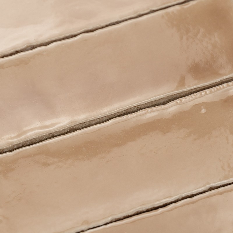 Azulejo cerámico rectangular beige brillante con juntas oscuras; varias piezas similares adyacentes forman un patrón diagonal.