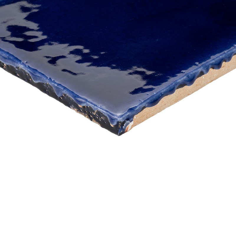 Bright blue ceramic tile, irregular glazed edge and exposed ceramic body edge; cut corner on white background.