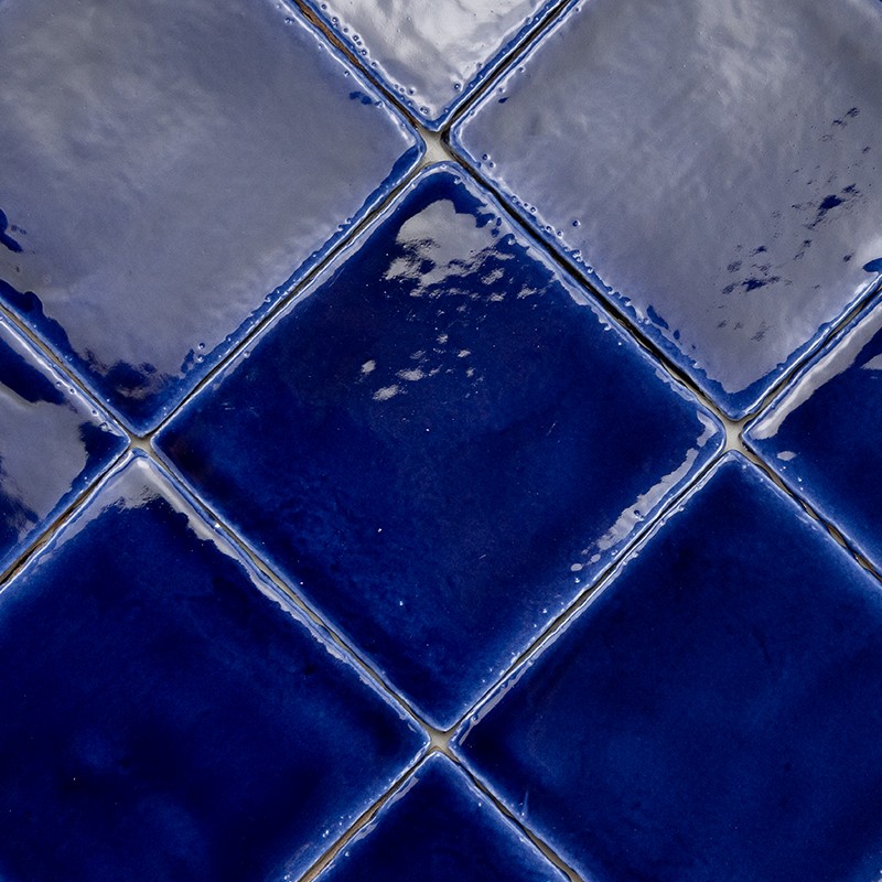 Cobalt blue ceramic tiles arranged in rhombuses; glazed gloss with reflections and tonal variations, light joints and small imperfections near the corners.