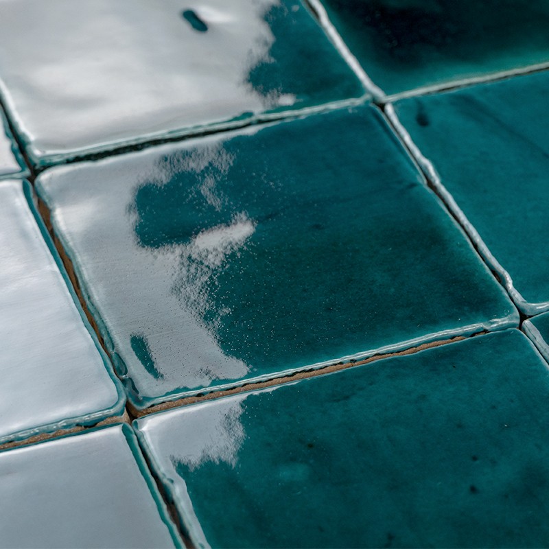Bright turquoise glazed tile; several adjacent tiles with clear grout lines, reflective surface showing white reflections and dark variations.