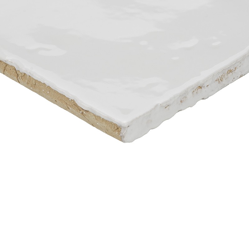 Witte geglazuurde tegel, hoek met onregelmatige, licht beschadigde rand; onderzijde beige keramisch karkas zichtbaar; glossy bovenlaag reflecteert licht, tegen neutrale witte achtergrond.