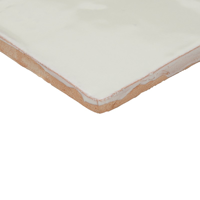 Azulejo branco esmaltado, canto inferior mostrando camada de cerâmica e rejunte descascado; superfície brilhante, fundo neutro branco.
