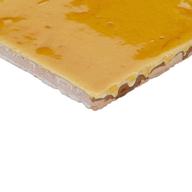 Gelb glasierte Keramikfliese, nahes Eckdetail mit unregelmäßiger Glasuroberfläche und sichtbarer gebrannter Scherbenkante, freigestellt vor weißem Hintergrund.