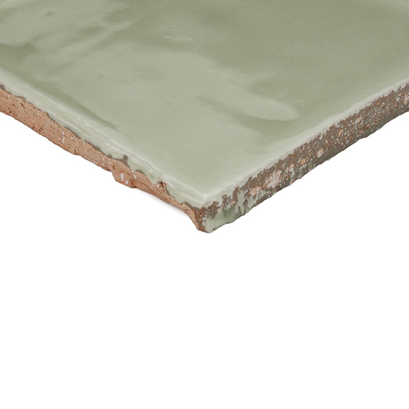 Pale green glazed rectangular tile with worn lower edge revealing clay base; on a neutral white background.