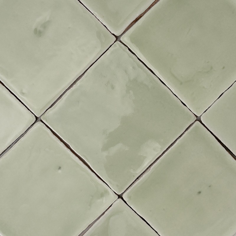Pale green square tile with glossy glaze and small irregularities; surrounded by similar tiles joined by dark joints forming a diagonal pattern.