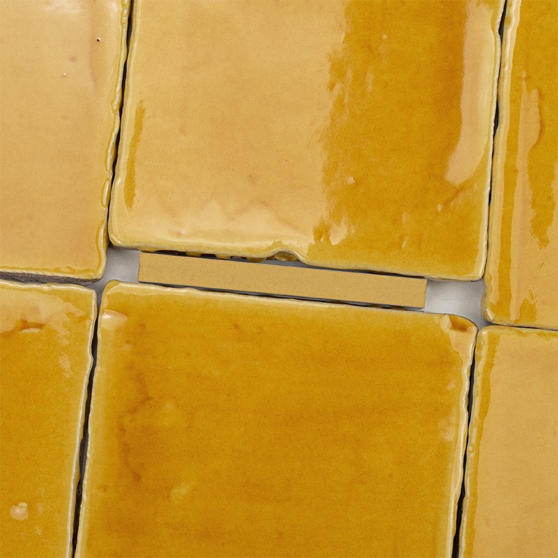 Square ceramic tiles, yellow-amber, glazed and glossy; visible gray joints with small gaps between pieces and slightly irregular edges.