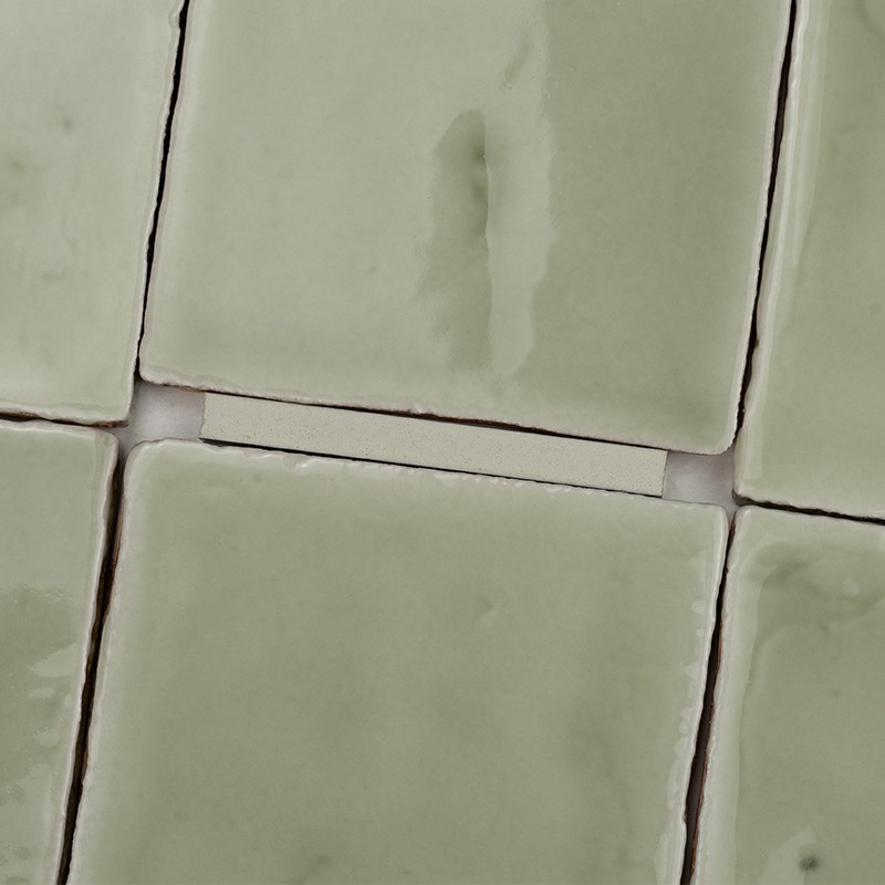 Square pale green ceramic tiles with glossy glaze and small imperfections; narrow joints and visible white grout between the pieces.