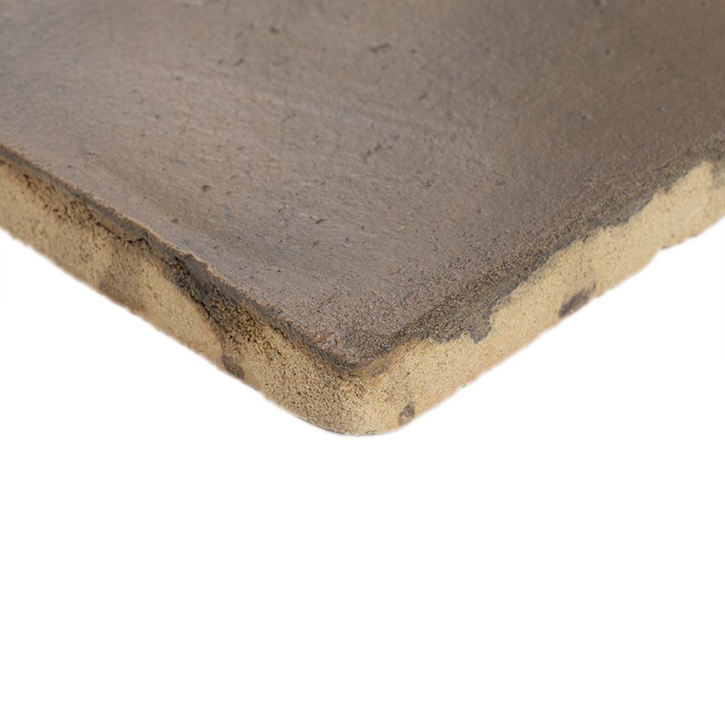 Ceramic tile with rounded edge and rough brown surface; underside reveals light core and glaze mixture, on neutral white background.