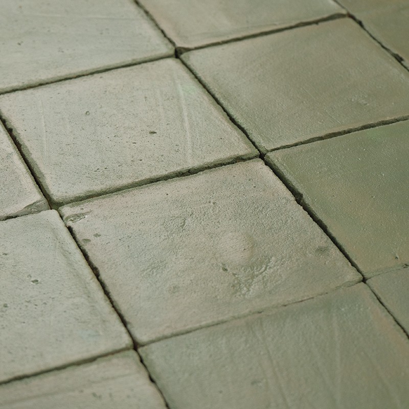 Groene keramische tegels met zichtbare voegen en lichte oppervlakteslijtage, geplaatst naast elkaar in een vlakke vloer.