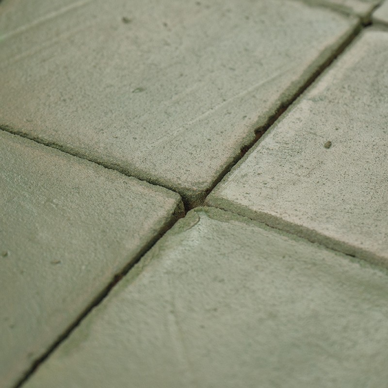 Carrelage quadrillé usé, quatre carreaux vert pâle aux bords arrondis et joints creusés; surface légèrement rugueuse et ébréchée, plan rapproché.