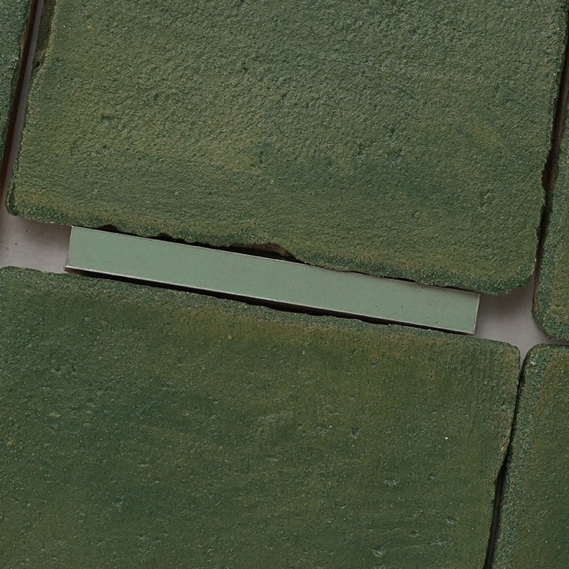 Rough and worn green tile (object); around, other similar tiles arranged in a narrow joint with a lighter rectangular piece between two tiles (context).