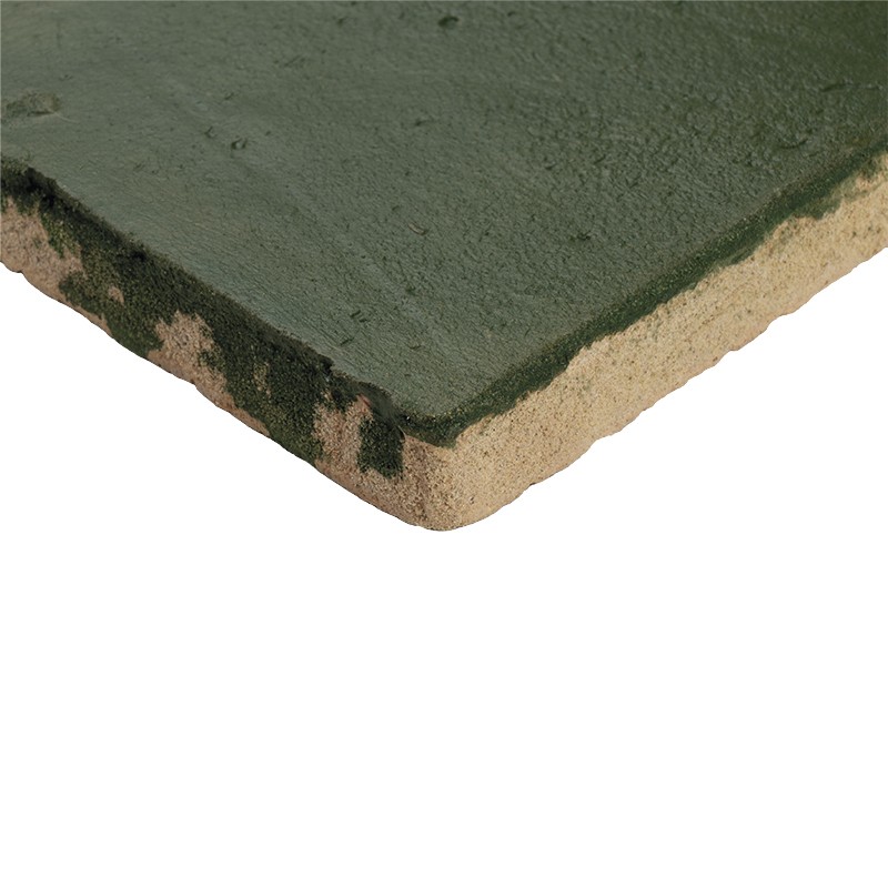 Azulejo cerámico verde con borde biselado y capa superior desgastada que revela sustrato arenoso beige; esquina recortada, marcas oscuras; aislado sobre fondo blanco.
