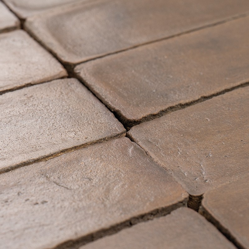 Carrelage rectangulaire brun côte à côte; joints foncés visibles, surfaces légèrement usées et rugueuses, bords irréguliers, gros plan montrant texture et petits espaces entre carreaux.