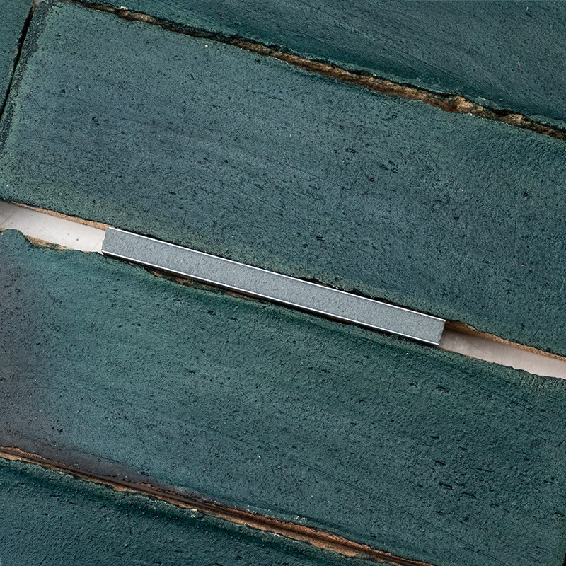 Groene rechthoekige keramische tegels met zichtbare donkere voegen; een smalle zilverkleurige metalen strip ligt in een horizontale voeg, witte ondergrond licht zichtbaar.