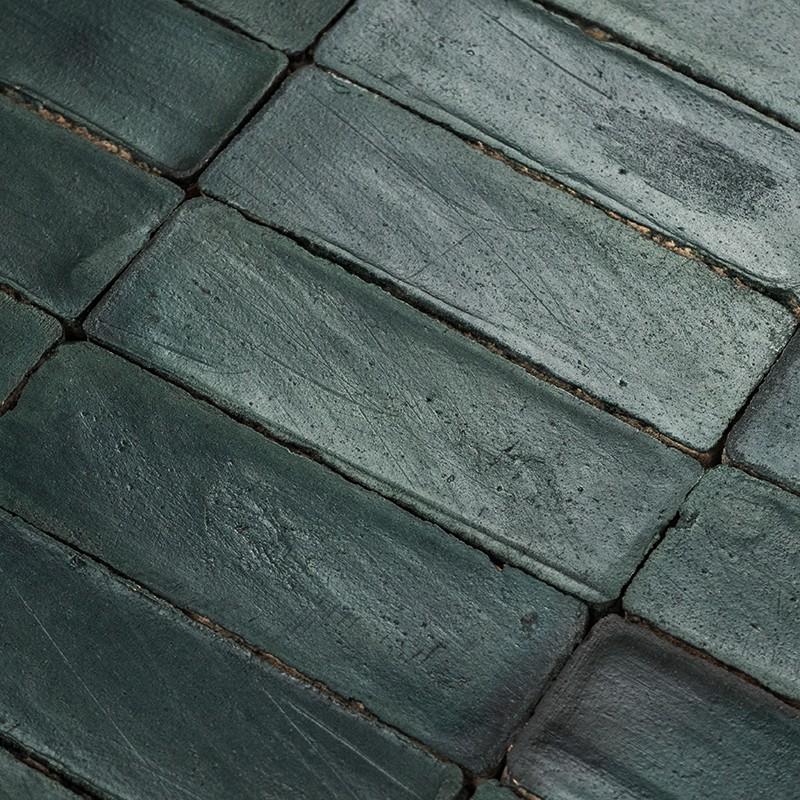 Dark green rectangular tiles with a rough surface and subtle sheen; narrow joints with dark grout; worn appearance, laid in a staggered pattern.