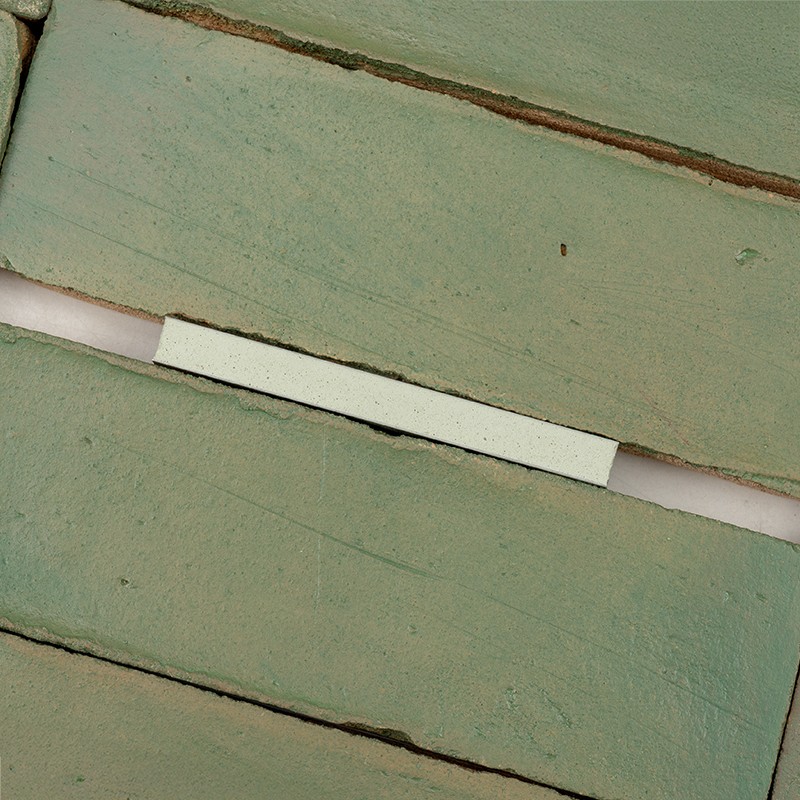Carrelage rectangulaire vert pâle: un espaceur blanc posé sur le joint exposé entre deux carreaux; surfaces légèrement éraflées et joints blancs visibles.