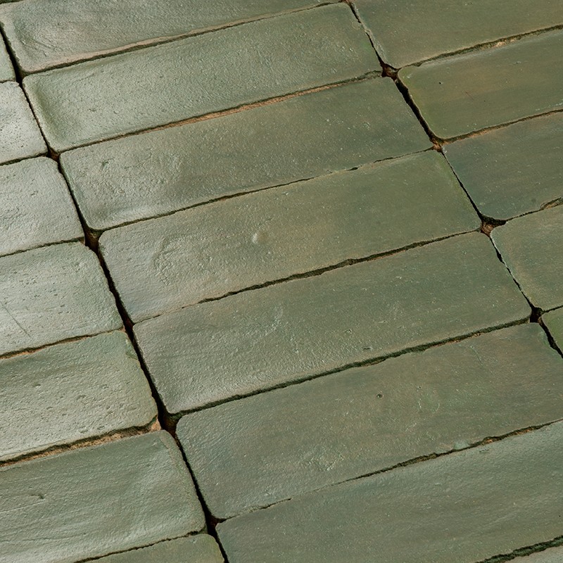 Groene rechthoekige tegels met lichte glans en slijtage, strak gelegd in rijen; smalle, donkere voegen en kleine chips zichtbaar tussen aangrenzende tegels.