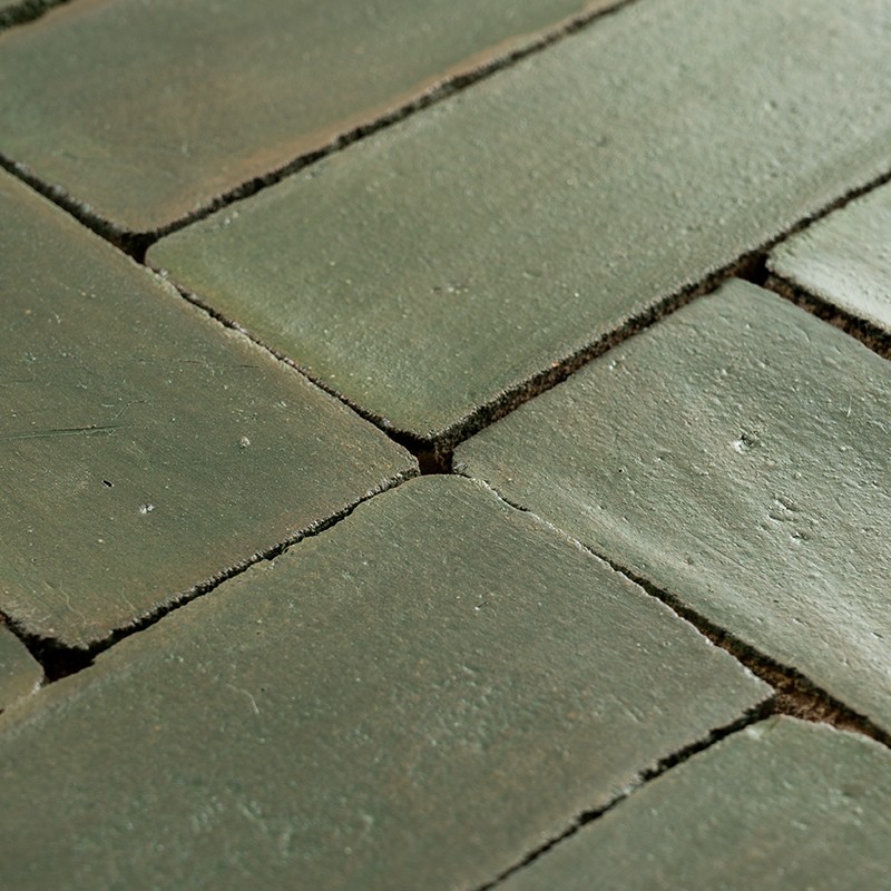 Carrelage rectangulaire vert mat; joints étroits de mortier foncé, surfaces légèrement irrégulières et usées.