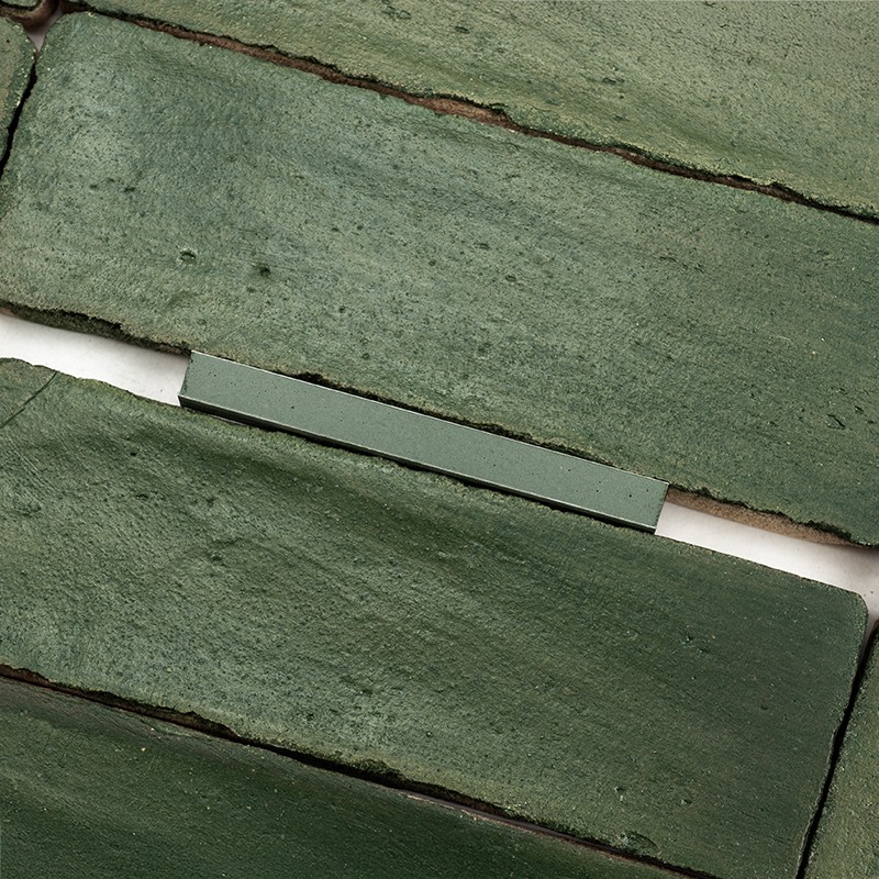 Rectangular green tiles, matte glazed and rough textured; arranged horizontally with visible white joints and irregular edges, appear to be placed on a neutral surface.