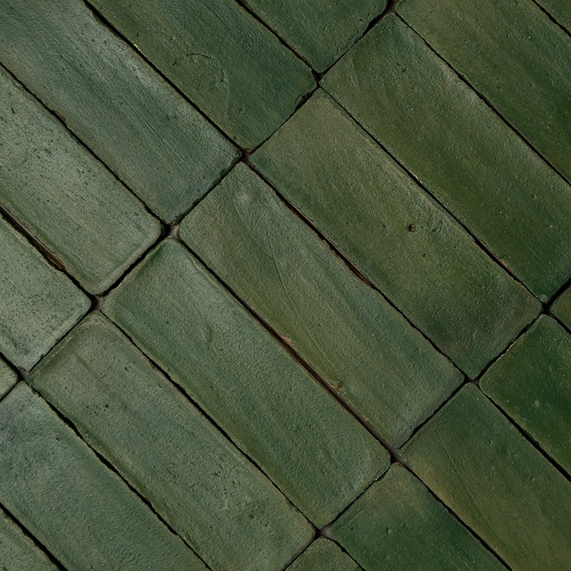 Azulejos cerâmicos verdes retangulares dispostos em padrão diagonal; juntas escuras, superfícies levemente irregulares e brilho fosco, aparência envelhecida.