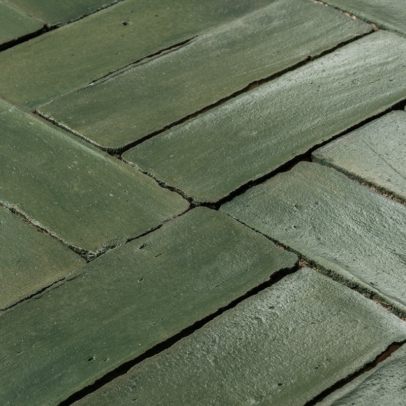 Green glazed rectangular tile as the focal point; surrounded by similar pieces in a staggered pattern with dark joints, irregular surface and subtle shine.