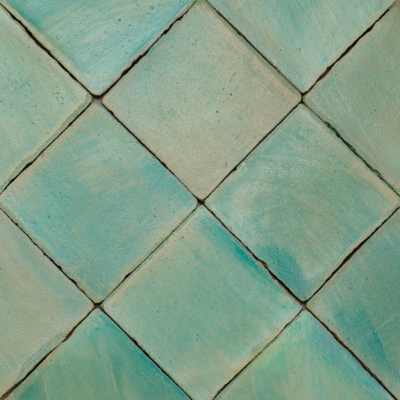 Carrelage de carreaux céramiques losangés bleu-vert légèrement irréguliers, joints sombres visibles; surfaces mates avec nuances et fines fissures, disposés en motif diagonal serré.
