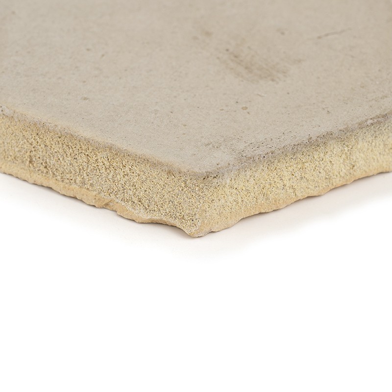 Beige ceramic tile cut at a corner, smooth surface with a slight texture and porous lower edge; resting on a white background, uniform light highlighting the edge and thickness.