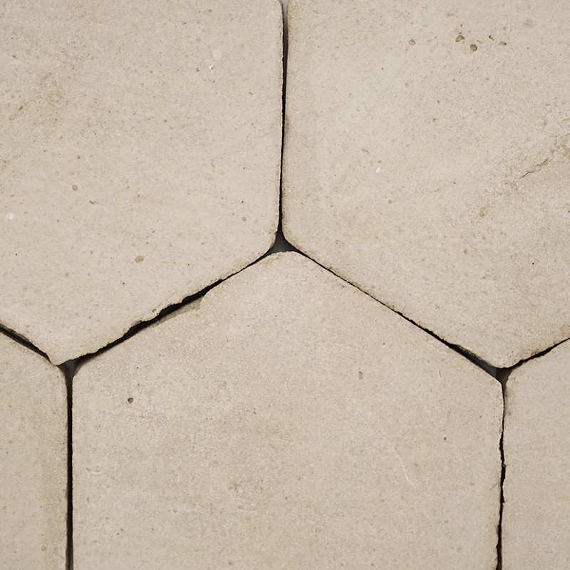 Beige hexagonal tile, smooth surface with small speckles; dark joints that form points where three pieces meet, continuous mosaic placement on floor or wall.
