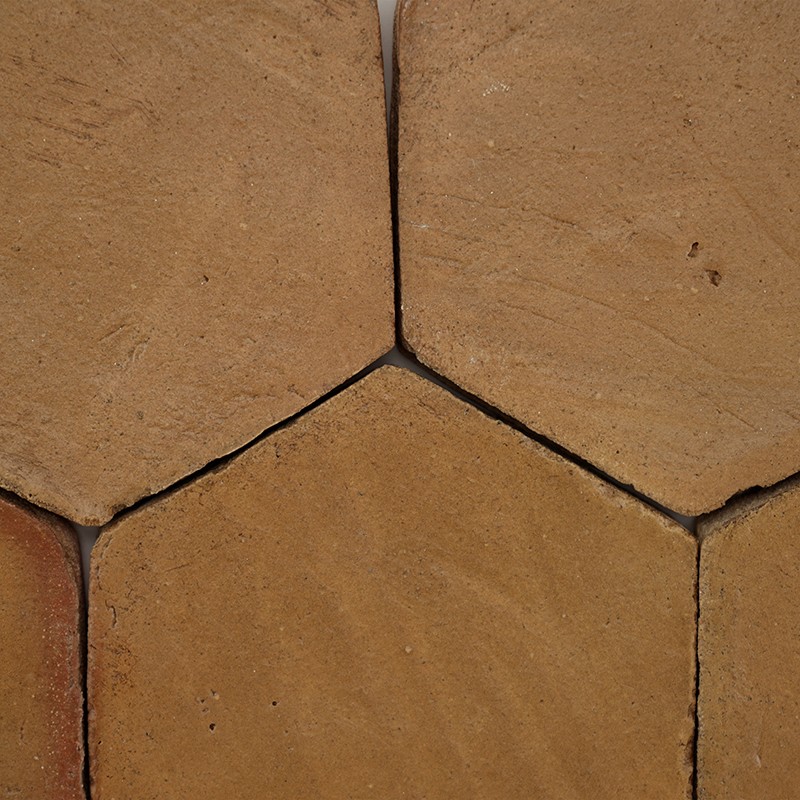 Hexagonal tile of ochre-colored clay, smooth surface with veins; context: other adjacent hexagonal tiles and dark joints forming a Y-shaped union.