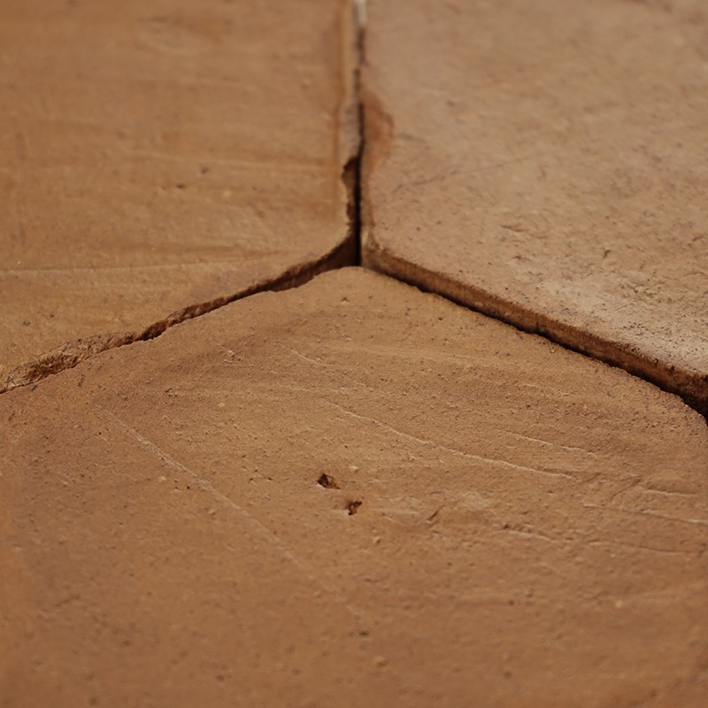 Chipped terracotta tile, three-piece junction with joints and cracks; matte surface with signs of use, installed on a rustic-style floor.