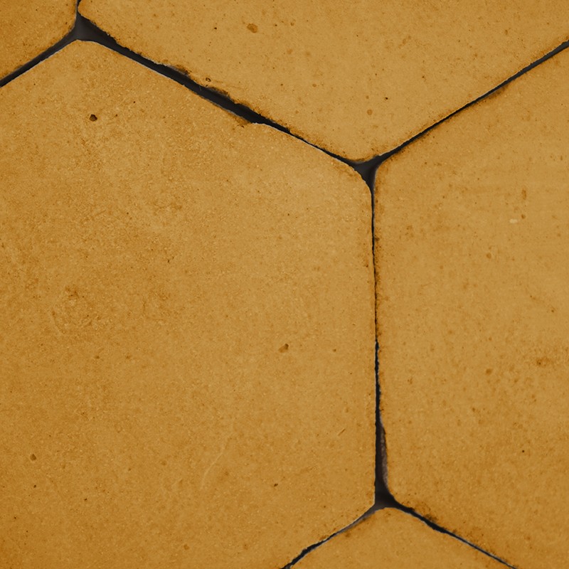 Azulejo hexagonal amarillo desgastado; juntas negras agrietadas entre piezas, superficie ligeramente manchada y textura rugosa en un pavimento exterior.