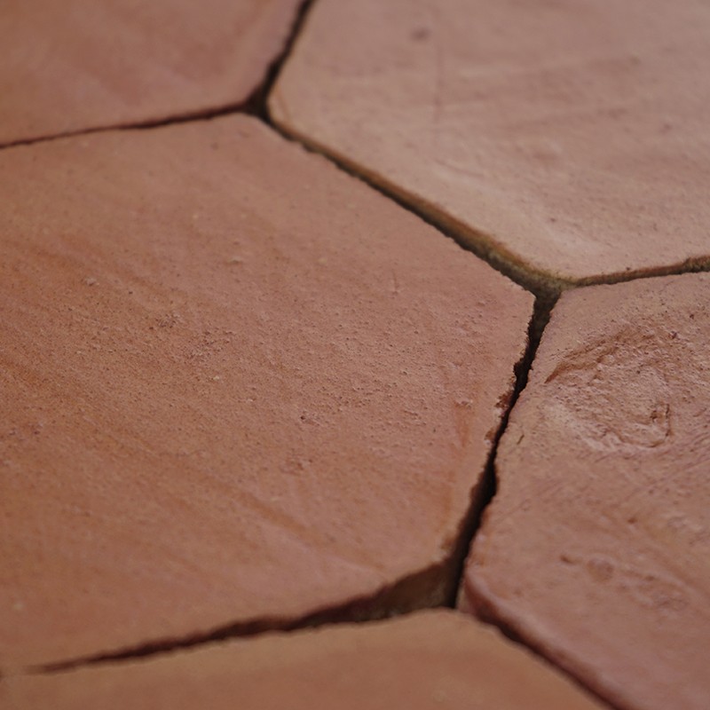 Azulejo hexagonal terracota en primer plano; juntas agrietadas y textura rugosa, rodeado de azulejos similares en un pavimento.