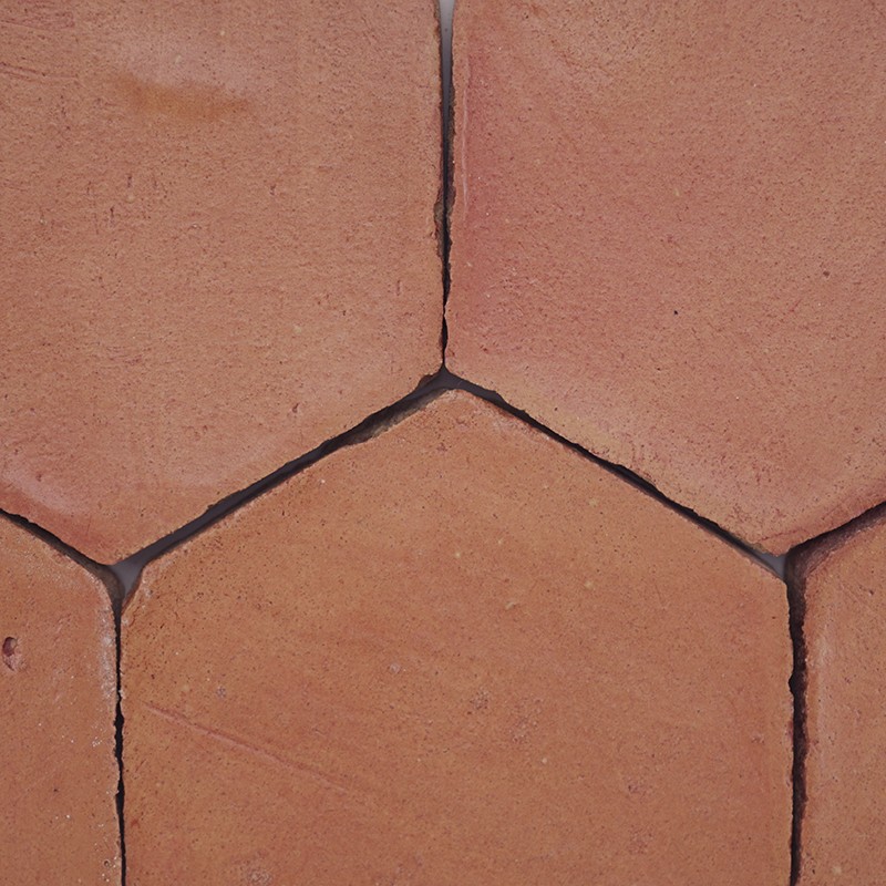 Azulejo hexagonal de terracota com juntas escuras e pequenas fissuras; superfície levemente desgastada, formando padrão contínuo no piso.
