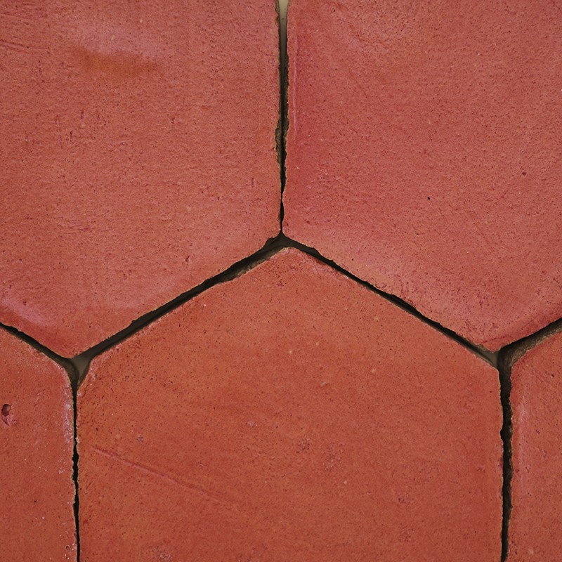 Azulejo hexagonal de terracota avermelhada, com juntas escuras e finas fissuras, formando um padrão repetido de piso ou parede rústica.