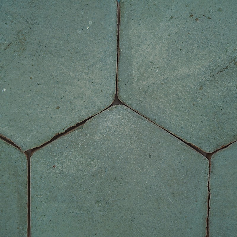 Grayish-green hexagonal tiles with dark grout lines; rough floor pattern with small cracks and a slightly worn appearance.
