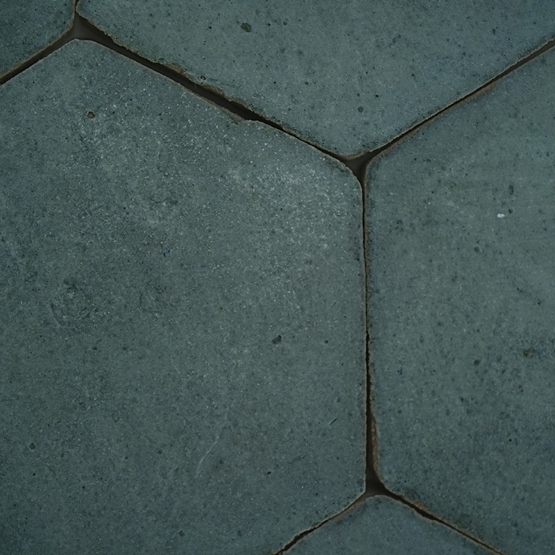 Carrelage hexagonal gris: dalles en béton aux bords arrondis, joints sombres et fins, surface granuleuse parsemée de petites taches.