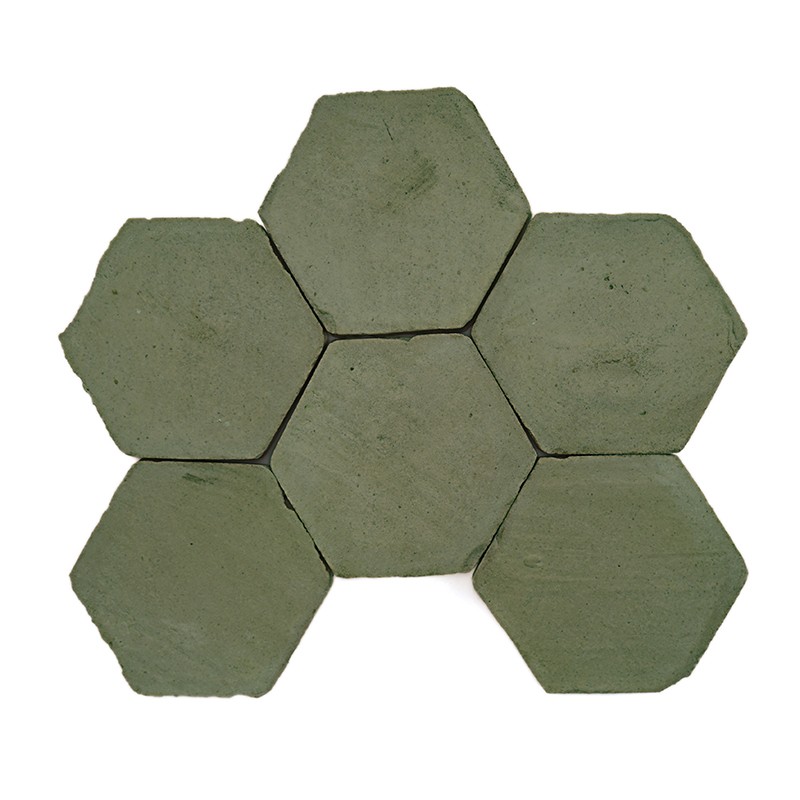 Azulejo hexagonal verde grisáceo, superficie ligeramente desgastada con pequeñas manchas y bordes algo irregulares; sobre fondo blanco liso.